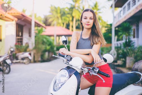 Riding lifestyle. Outdoor portrait of pretty young woman in shorts sitting on scooter. © luengo_ua