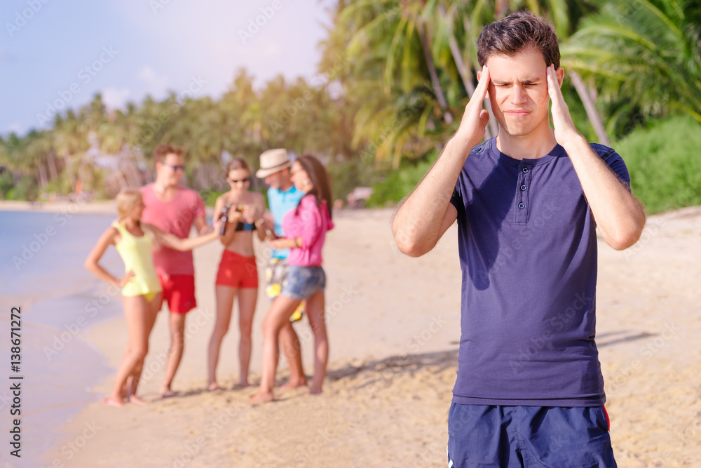 Stress and headache. Young man feeling bad while his friend enjoying beach party. Stress and headache. Young man feeling bad while his friend enjoying beach party.