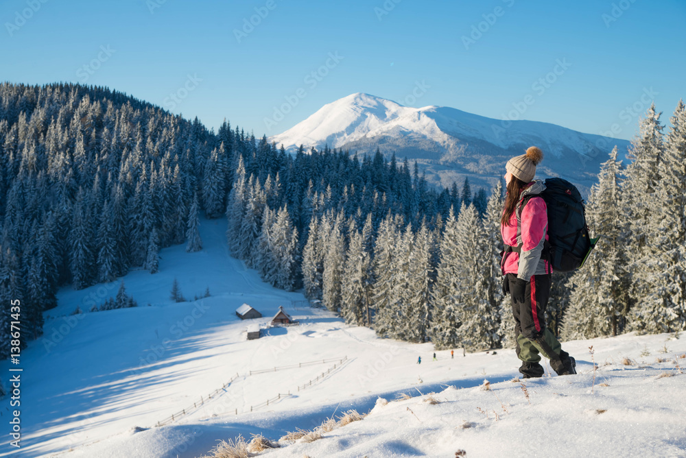 Happy young woman with a backpack standing on snow  and looking into the mountains