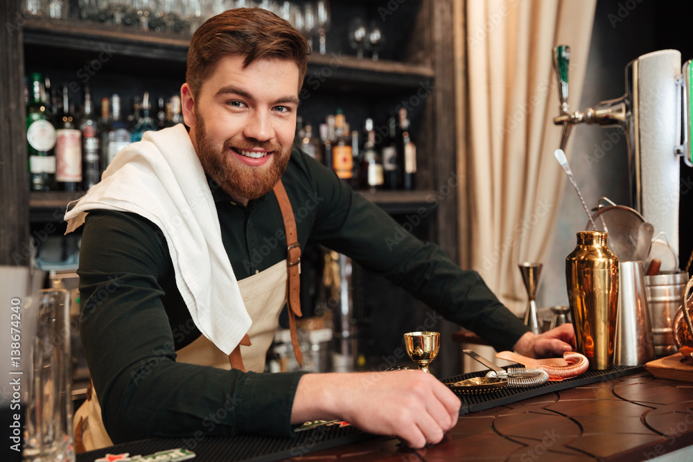 Cheerful young bearded man bartender standing in cafe.