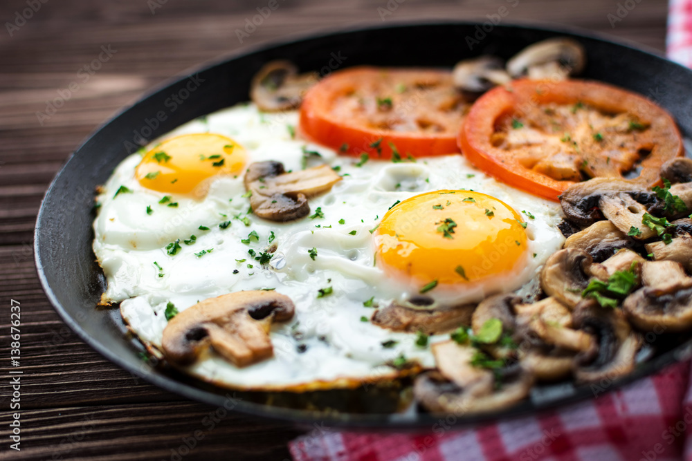 Fried eggs with mushrooms and tomato on dark wooden table Fried eggs with mushrooms and tomato on dark wooden table