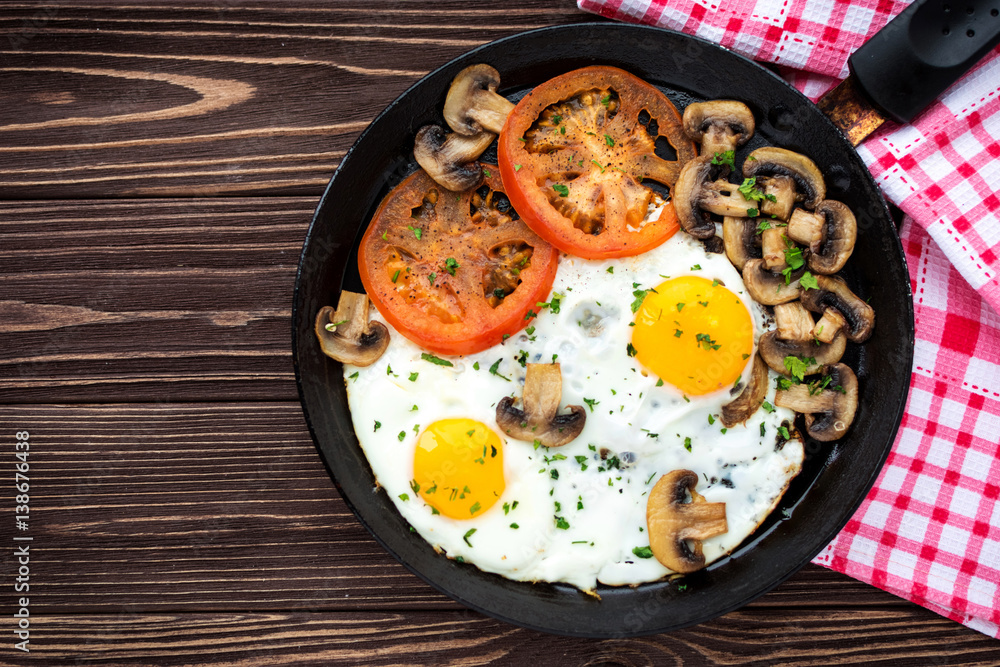 Fried eggs with mushrooms and tomato on dark wooden table Fried eggs with mushrooms and tomato on dark wooden table