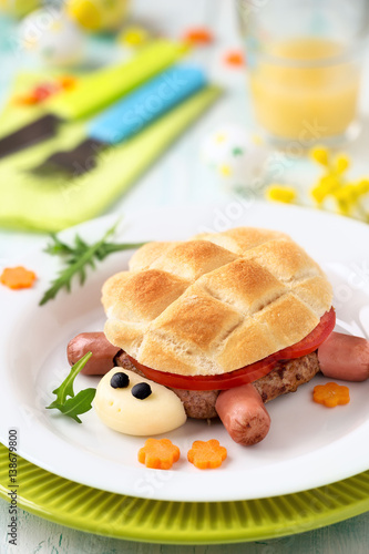 Fun food for kids - cute turtle shaped hamburger made of ground meat pattie, slices of fresh tomato and bread with Easter decoraions at the background photo