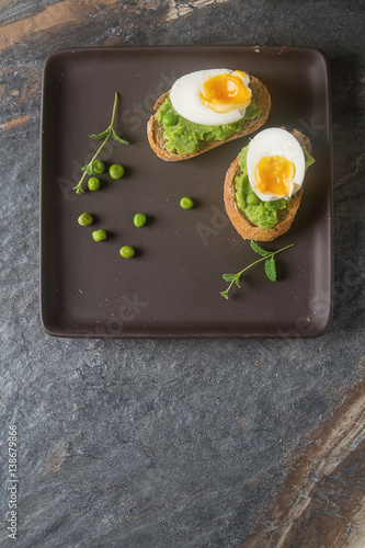 Baguette with mashed green peas, eggs and mint. Dark background.
