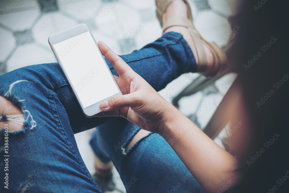 Mockup image of hand holding white mobile phone with blank white screen on thigh with a vintage tile floor in cafe , feeling relaxed