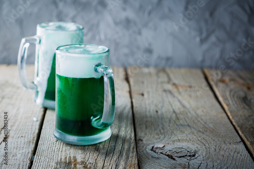 Green beer in mugs on rustic wood background