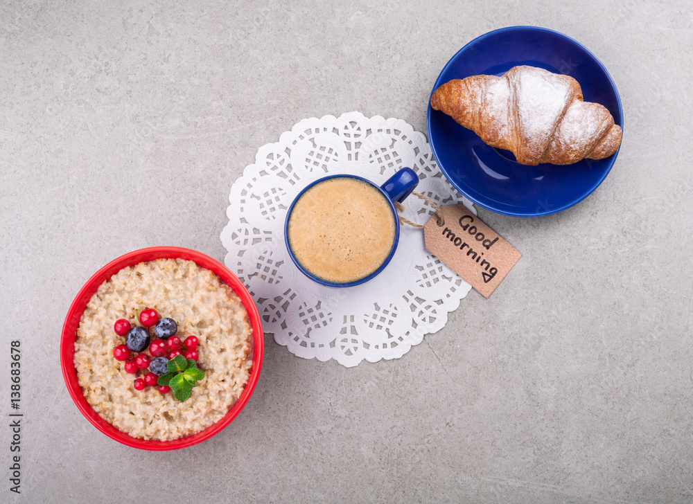 Coffee cup, oatmeal with berries, croissant and note good morning on grey background. Healthy breakfast concept. Top view. Copy space Coffee cup, oatmeal with berries, croissant and note good morning on grey background. Healthy breakfast concept. Top view. Copy space
