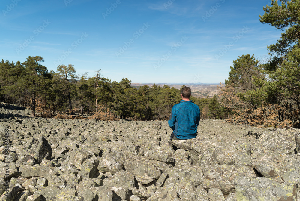 Hombre joven sentado en un lecho rocoso de un antiguo glaciar llamado río de piedras Hombre joven sentado en un lecho rocoso de un antiguo glaciar llamado río de piedras