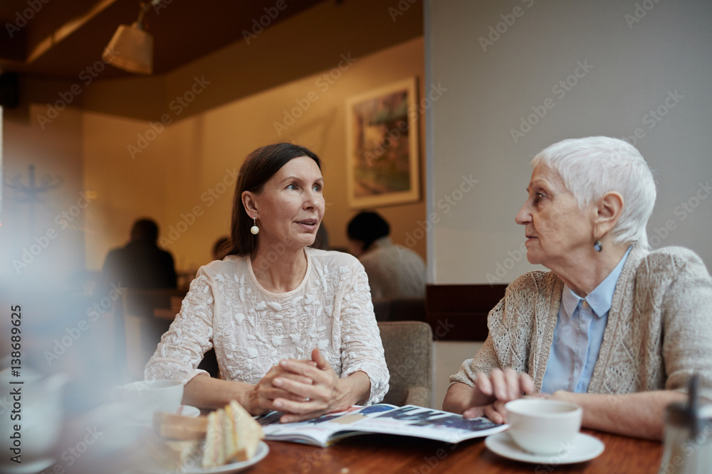 Friendly females with journal talking by table in cafe Friendly females with journal talking by table in cafe
