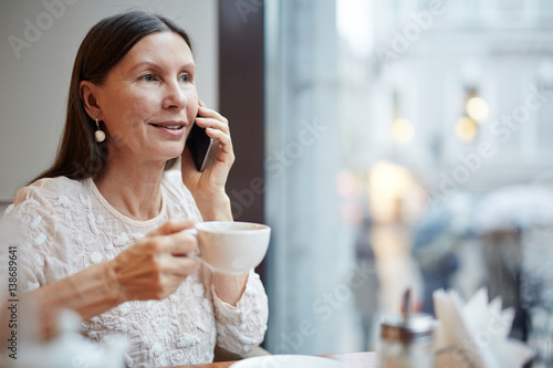 Mature female with cup of tea speaking on her smartphone