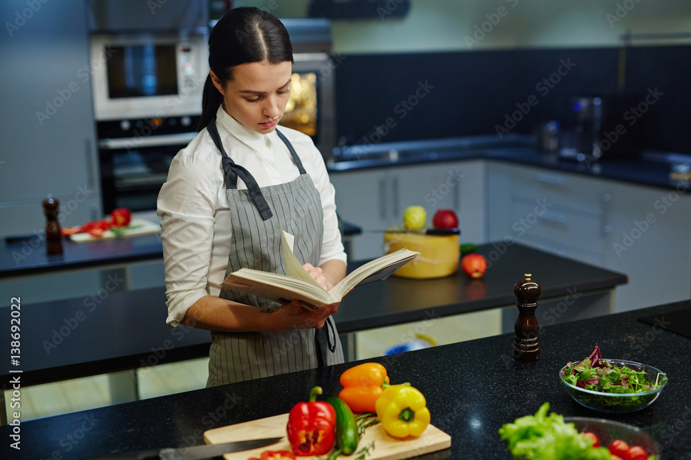 Fototapeta premium Housewife reading recipe in cookery book
