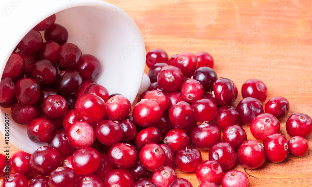 White cup from spilling out of it cranberries on a wooden background White cup from spilling out of it cranberries on a wooden background