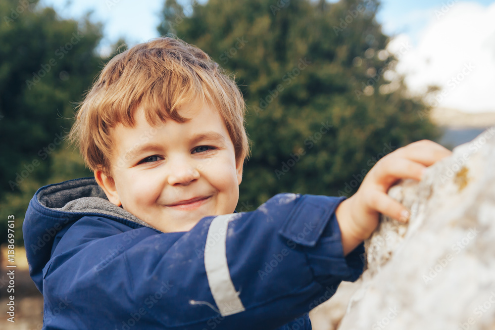 Close-up portrait 6 year old boy wearing jacket, happy smile on his face, blue eyes, blonde hair, rocks in nature Close-up portrait 6 year old boy wearing jacket, happy smile on his face, blue eyes, blonde hair, rocks in nature