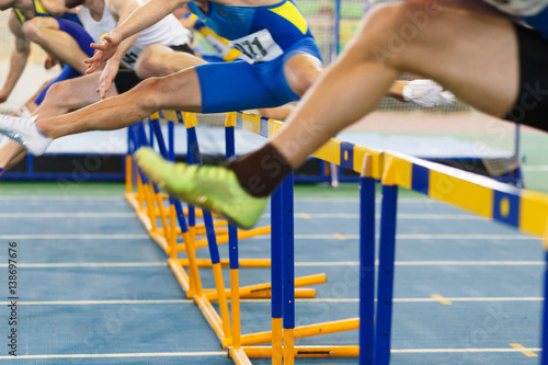 sportsmen running hurdles sprint race in indoor track and field competition photo