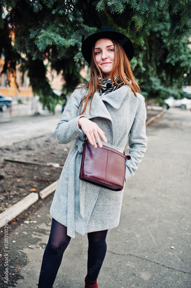 Young model girl in a gray coat and black hat with leather handbag on shoulders posed on street of city. Young model girl in a gray coat and black hat with leather handbag on shoulders posed on street of city.