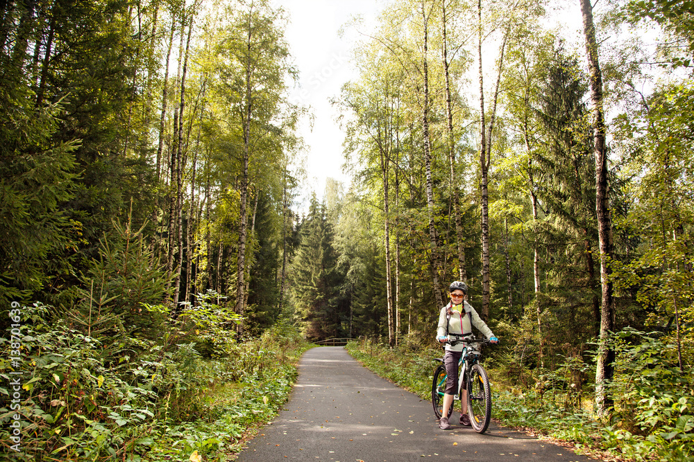 Female tourist cyclist  standing on road in forest, looking to camera and smiling.