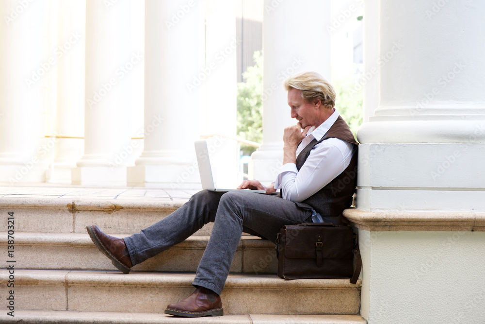 man sitting outdoors on steps and working on laptop