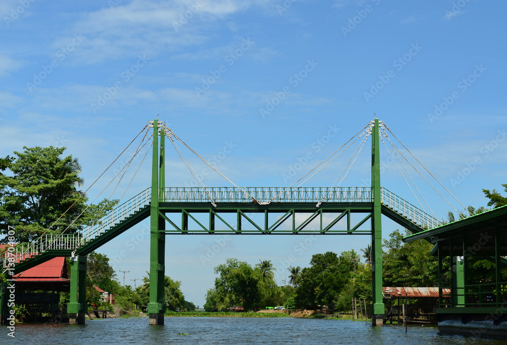 Green sling iron bridge over canal and blue sky