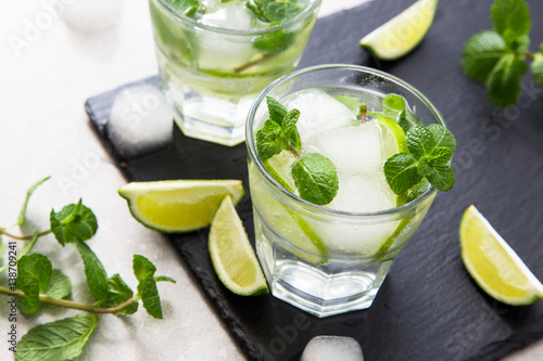 Cold refreshing summer lemonade mojito in a glass on a slate board and stone background.