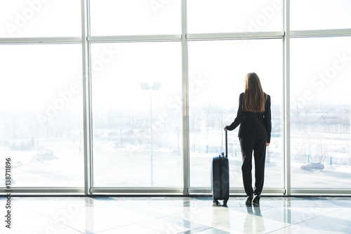 Businesswoman in airport with laggage looking at terminal panoramic windows