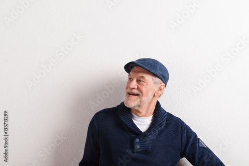 Senior man in sweater and cap, studio shot.