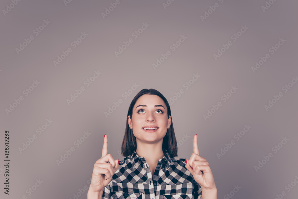 Portrait of young smiling happy woman pointing up against gray background Portrait of young smiling happy woman pointing up against gray background