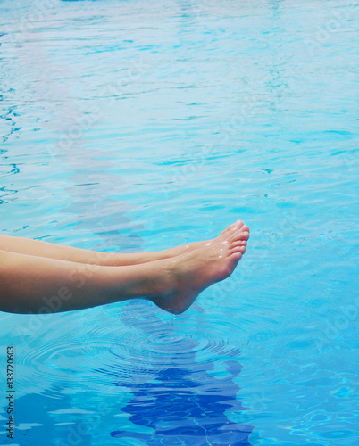 Woman's feet against blue water of the pool. Feet in the pool 