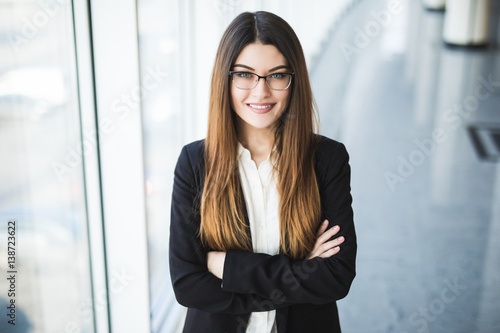 Businesswoman crossed hands portrait in office with panormic windows.