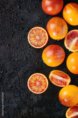 Sliced and whole ripe juicy Sicilian Blood oranges fruits on black wet metal texture background. Top view with space