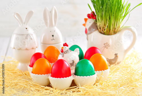 Easter eggs colored with organic paints and plate in the form of chickens and rabbits on a white wooden background.