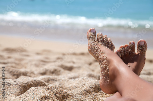 Woman tanned legs on sand beach.