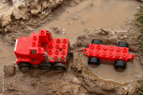 A child playing with a red car in the mud puddle.