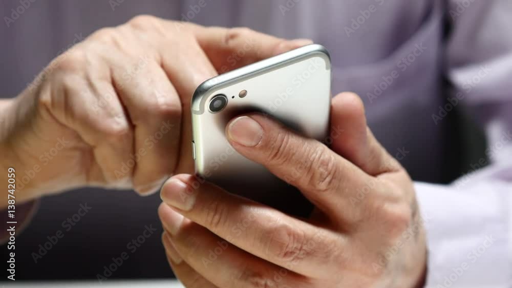 Elderly Man Text Messaging On Smartphone While Sitting At The Table Elderly Man Text Messaging On Smartphone While Sitting At The Table