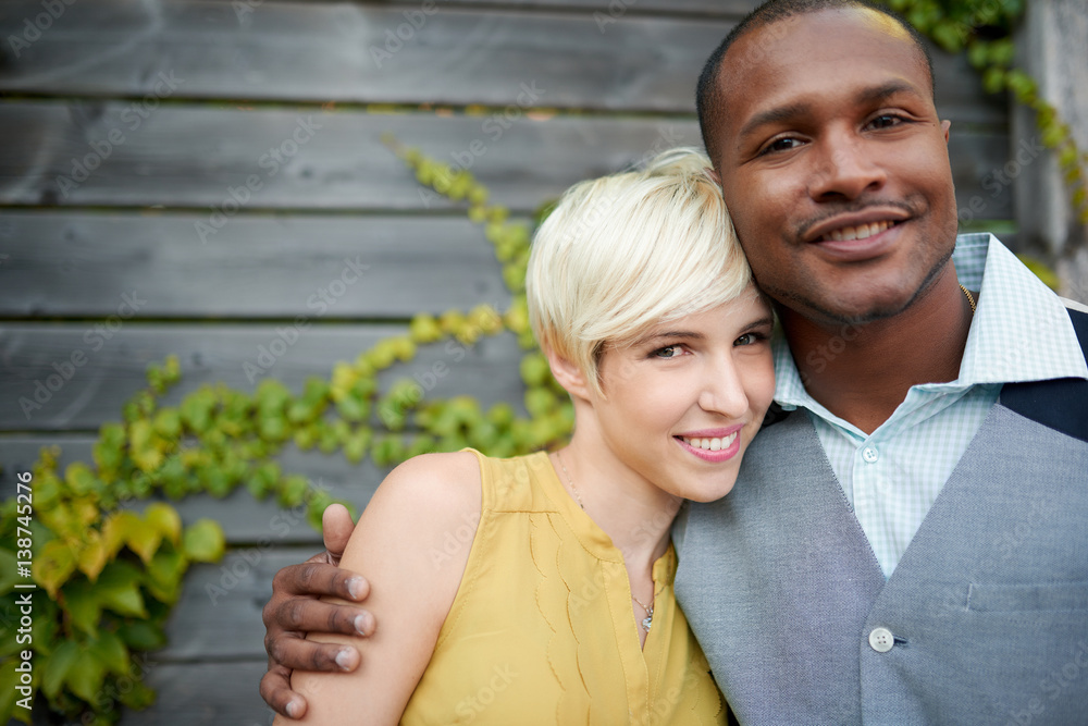 Attractive and stylish multicultural couple in love cuddling by a fence in an ivy-filled urban setting Attractive and stylish multicultural couple in love cuddling by a fence in an ivy-filled urban setting