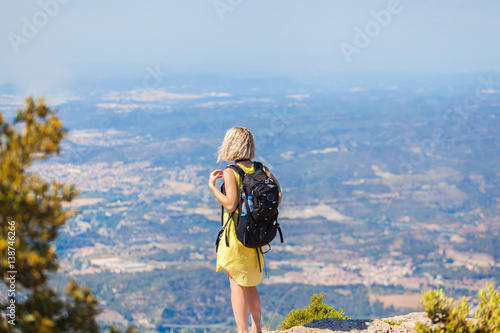 Female traveler with a backpack on her back enjoying the views from the mountains of Montserrat in Spain. The girl in a yellow dress on background of the nature