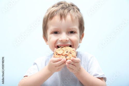 Cute little boy eating cookie on light background