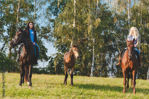 Two female equestrians with purebred brown horses and foal between them.