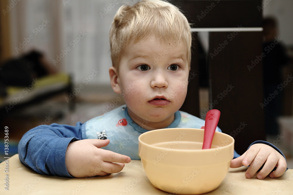 Wonder struck boy by the empty brown saucer with pink spoon Wonder struck boy by the empty brown saucer with pink spoon