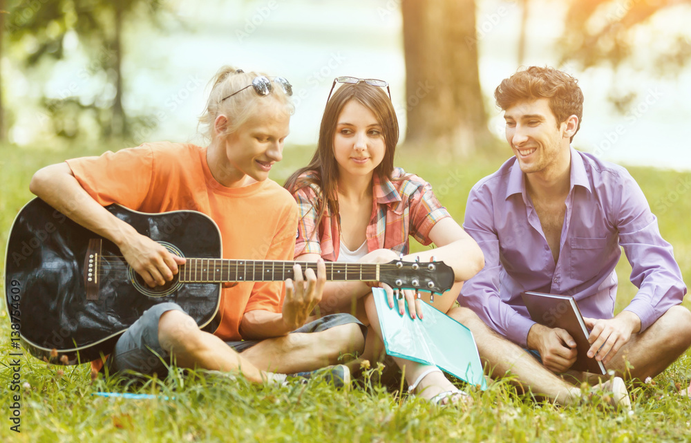 group of students with a guitar resting in the Park on a Sunny day
