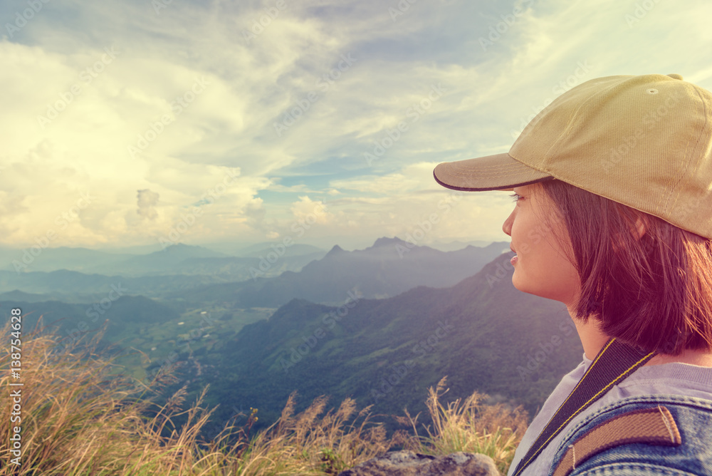 Vintage style hiker asian teen girl wear cap with happy looking beautiful landscape nature on top of high mountain at viewpoint Phu Chi Fa Forest Park, Chiang Rai, Thailand