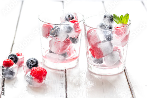 Ice cubes with blueberry and raspberry in glass on wooden table