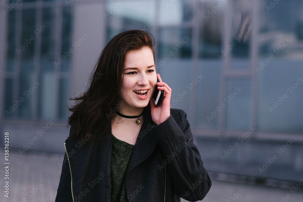 portrait of a happy and stylishly dressed woman is talking on the phone on a city a dark background