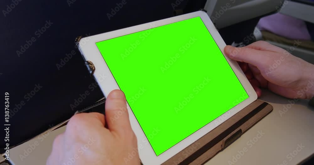 An airplane passenger uses a green screen tablet PC at his seat. Green screen with optional tracking points for advanced screen replacement. An airplane passenger uses a green screen tablet PC at his seat. Green screen with optional tracking points for advanced screen replacement.
