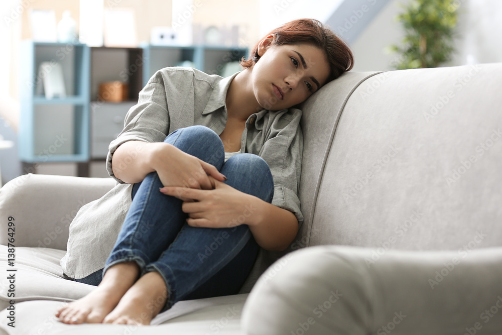 Depressed young woman sitting on sofa at home Depressed young woman sitting on sofa at home