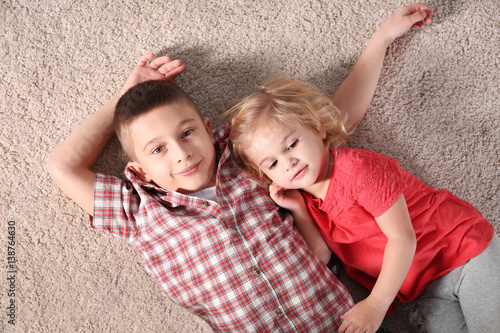 Cute little brother and sister lying on soft carpet
