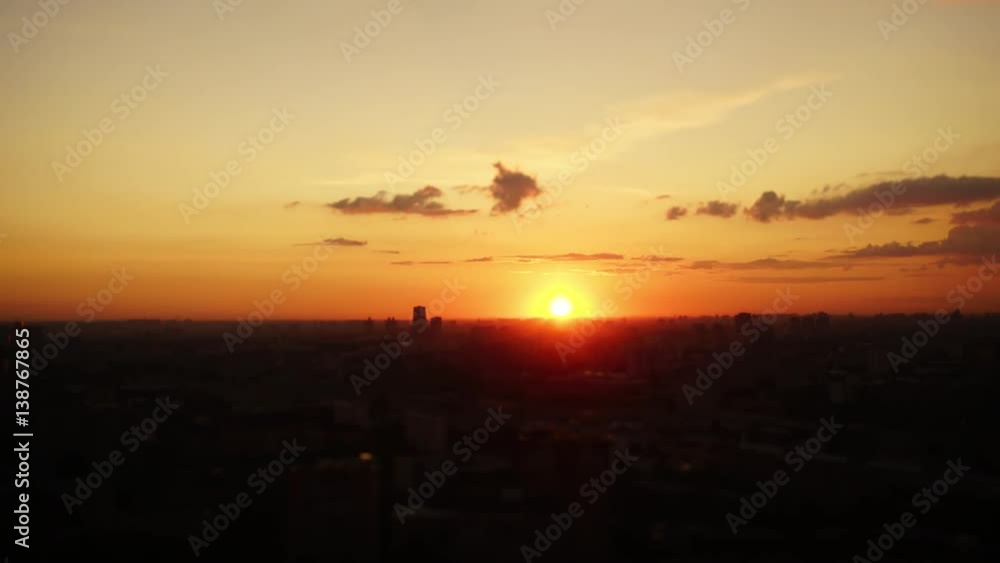 Time lapse tilt shift shooting from high above of summer evening and nightfall in big modern city with blurred silhouettes of houses, the sun sets over the horizon, small clouds disappearing over time Time lapse tilt shift shooting from high above of summer evening and nightfall in big modern city with blurred silhouettes of houses, the sun sets over the horizon, small clouds disappearing over time