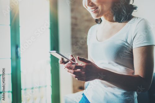 Young Asian woman using mobile phone at home on sunny sunday and holding smartphone on hands.Blurred background.