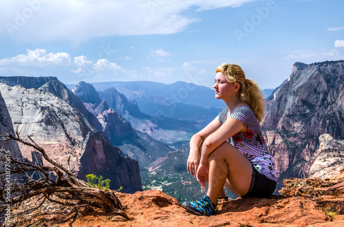 Young woman sitting on edge on top of canyon on Observation Point trail in Zion National Park