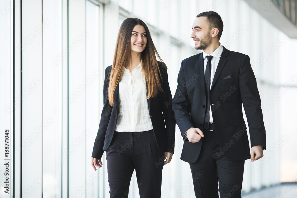 Confident business partners walking down in office and talking Confident business partners walking down in office and talking