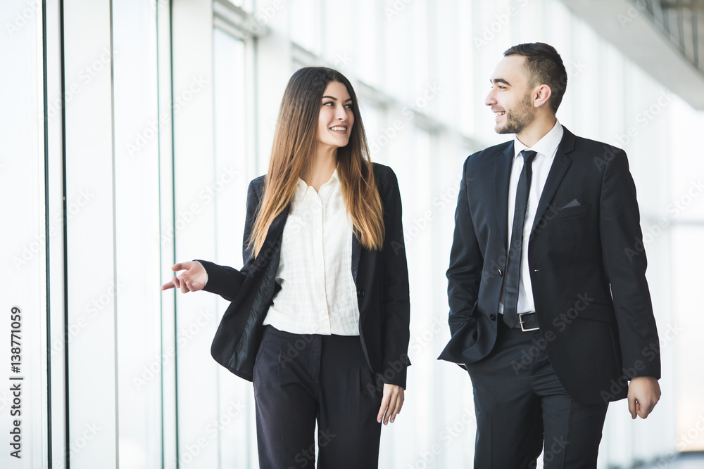 Confident business partners walking down in office and talking Confident business partners walking down in office and talking